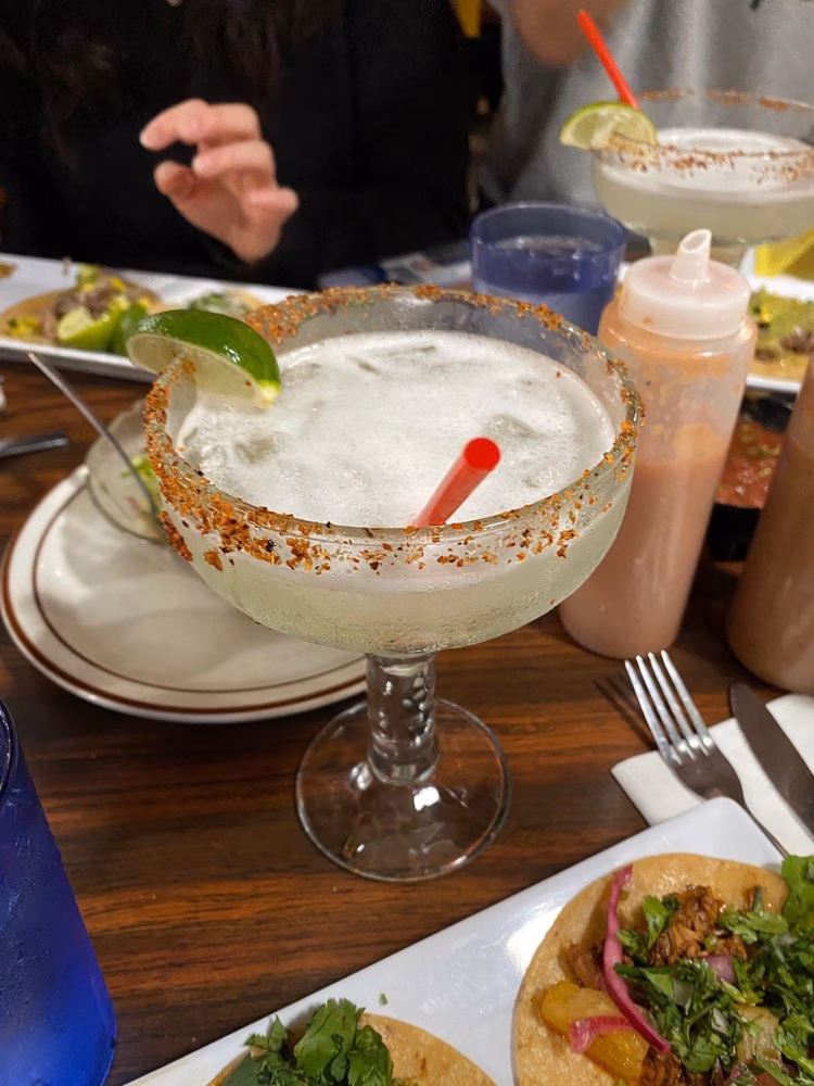 Frozen margarita with lime, red straw, and spiced rim on table.