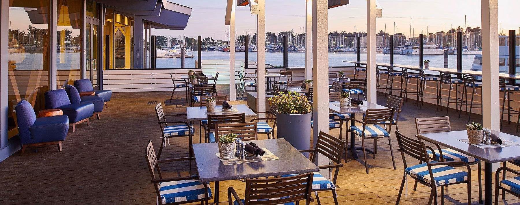 Waterfront restaurant patio with tables, chairs, and many boats.