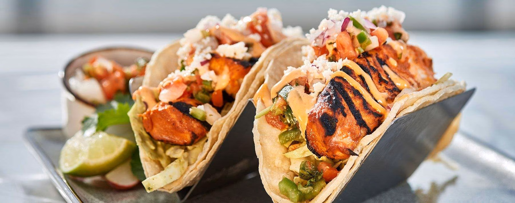 Two grilled tacos with salsa, cheese, and sauce on a serving plate.
