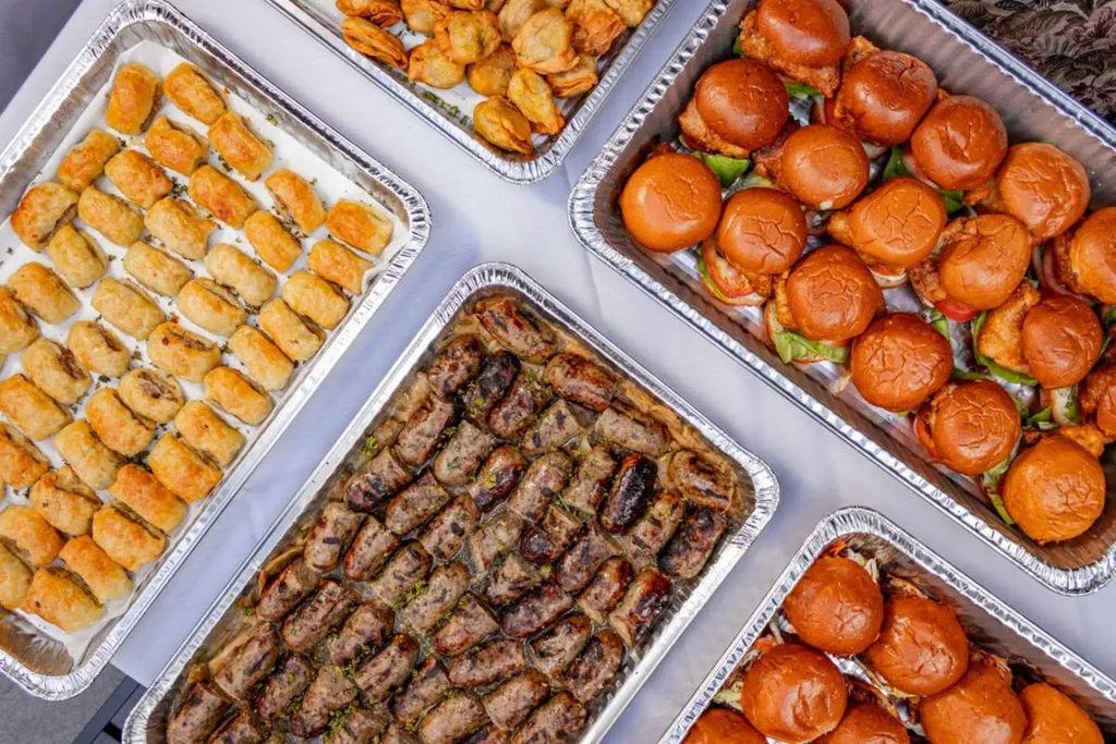 Various finger foods in silver foil catering trays.