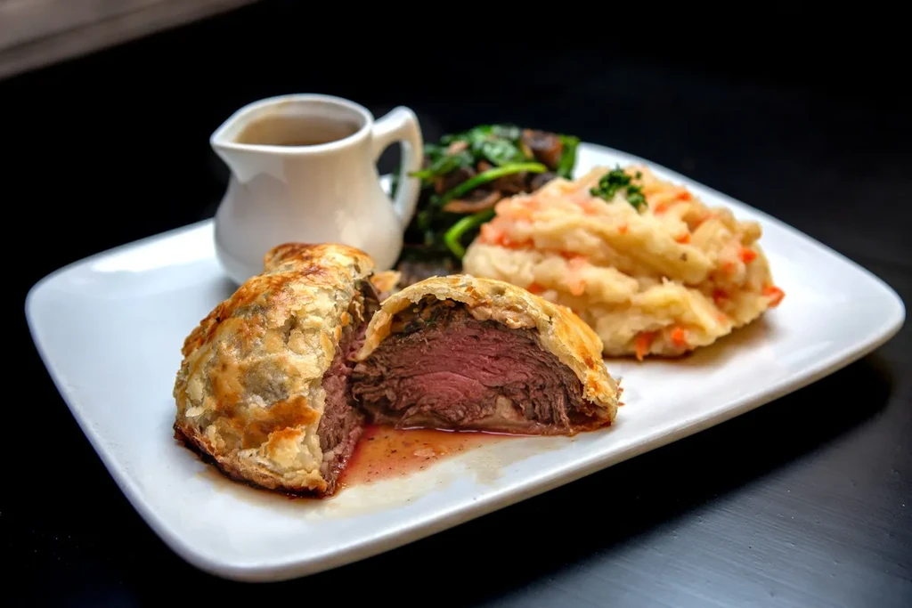 Sliced Beef Wellington, mashed potatoes, and vegetables on a plate.