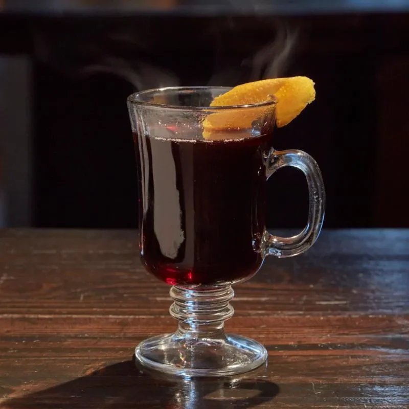 Clear mug of steaming reddish-purple drink with orange peel.