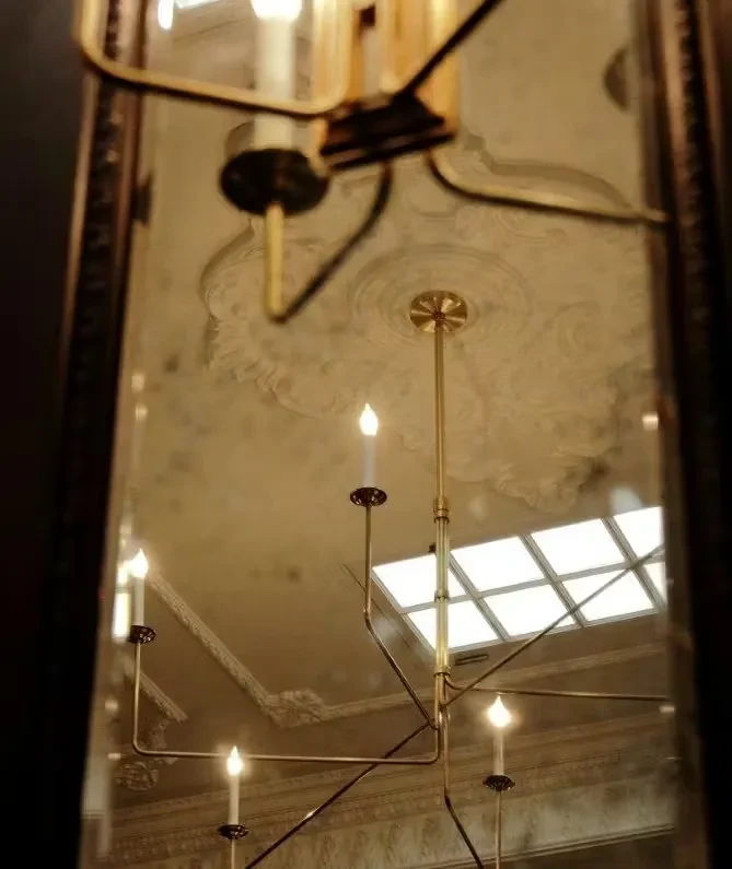 Ornate brass chandelier and decorative ceiling reflected in a mirror.