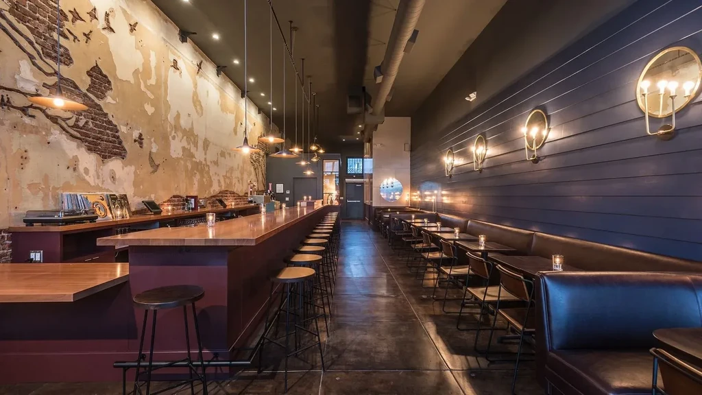 Rustic bar interior featuring a long counter, stools, and booth seating.