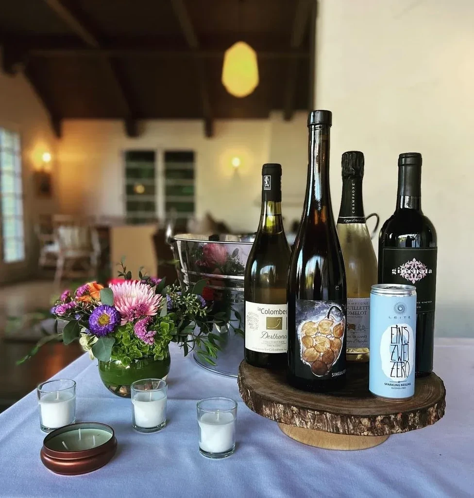 Restaurant table setting with wine bottles, flowers, and votive candles.