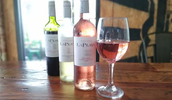 Three different wines and a rosé glass on a rustic wooden table.