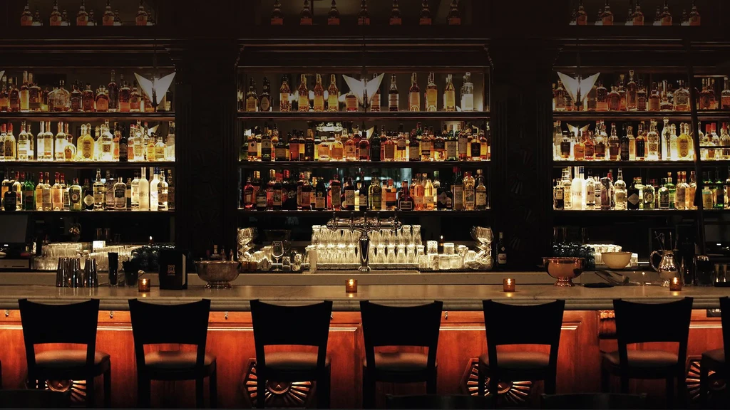 Extensive liquor bottle collection on illuminated shelves inside a dark bar.