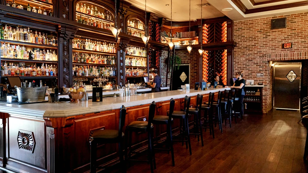 Luxurious bar interior with marble counter, liquor display, and three people.
