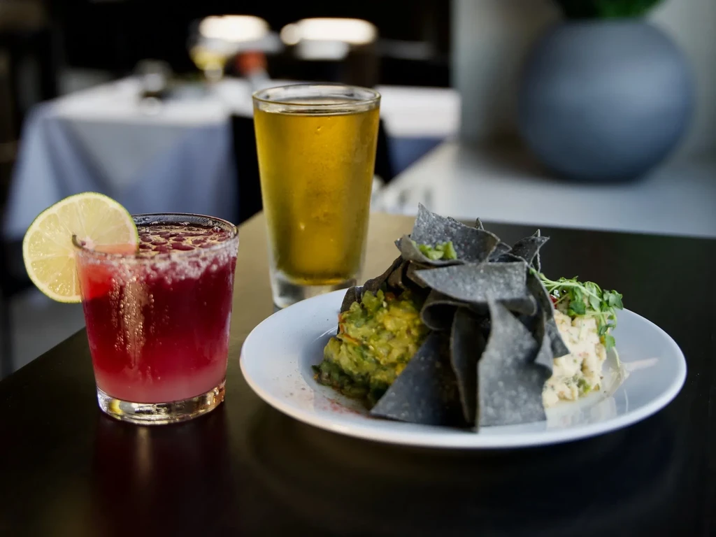 Red cocktail, golden beer, guacamole, chips on a restaurant table.