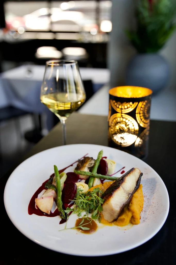 Plated seared fish, vegetables, wine, and candle in a restaurant.