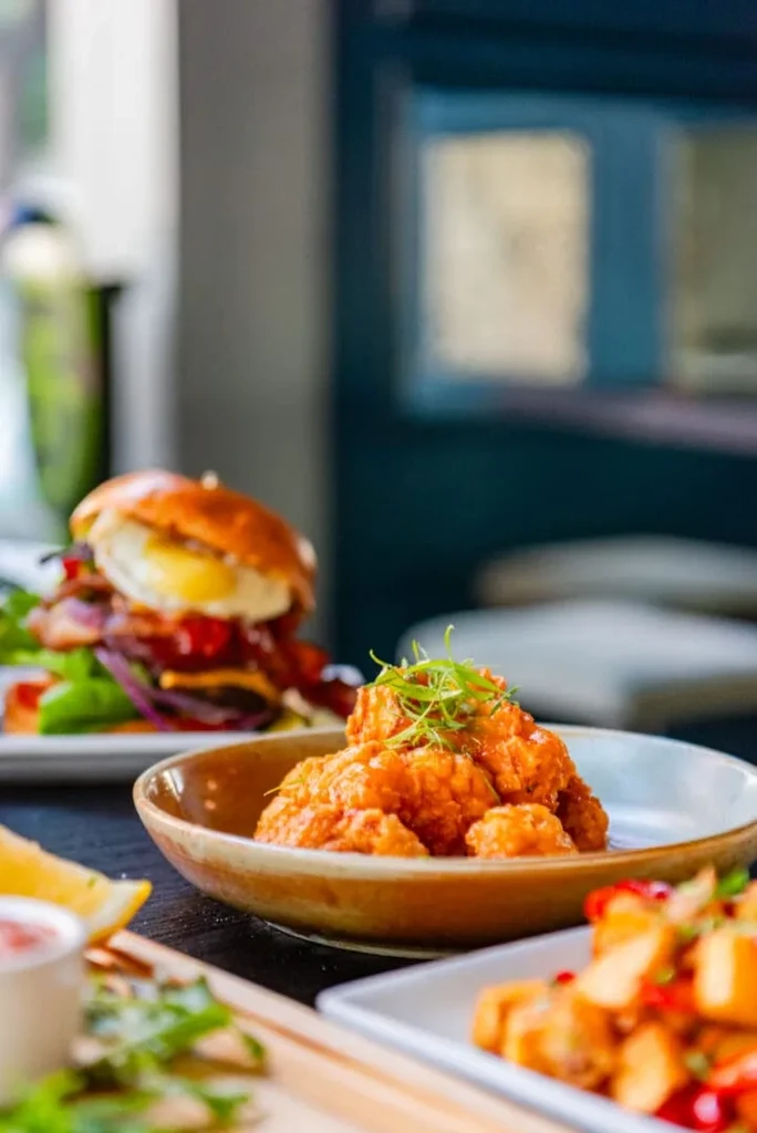 Crispy chicken bites, gourmet burger, and potatoes on a restaurant table.