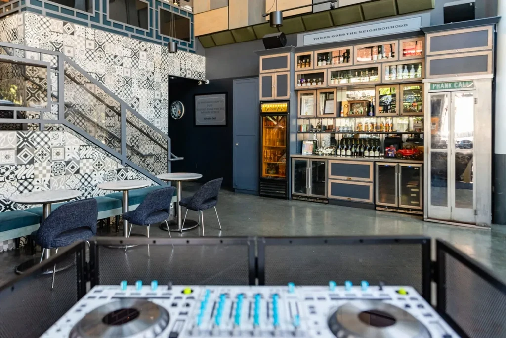 Modern bar interior: staircase, teal seating, stocked bar, and "Prank Call" booth.