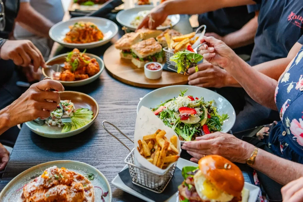 Hands reaching for diverse dishes including salad, fries, and ceviche.