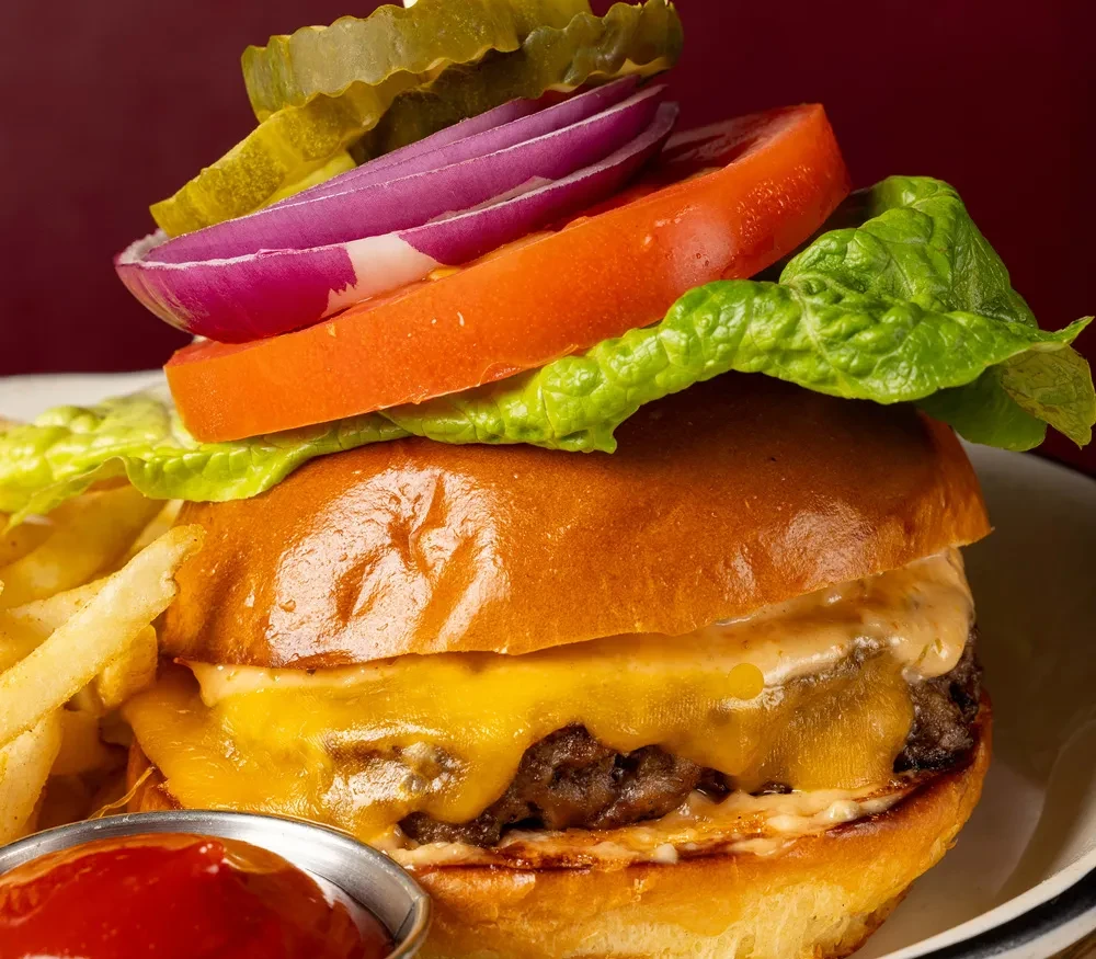 Stacked cheeseburger with fries and ketchup on a white plate.