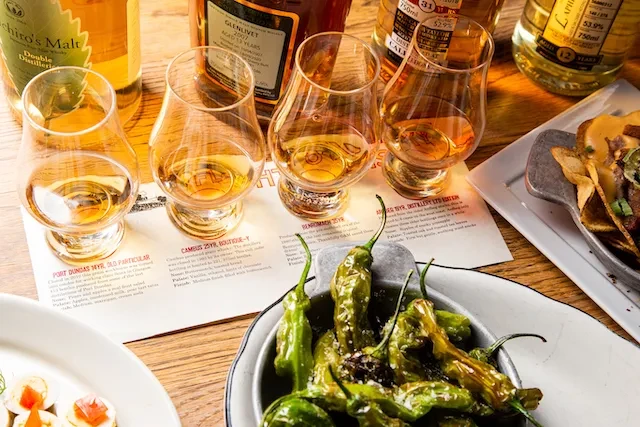 Overhead shot of a whisky tasting setup with glasses, bottles, and food.