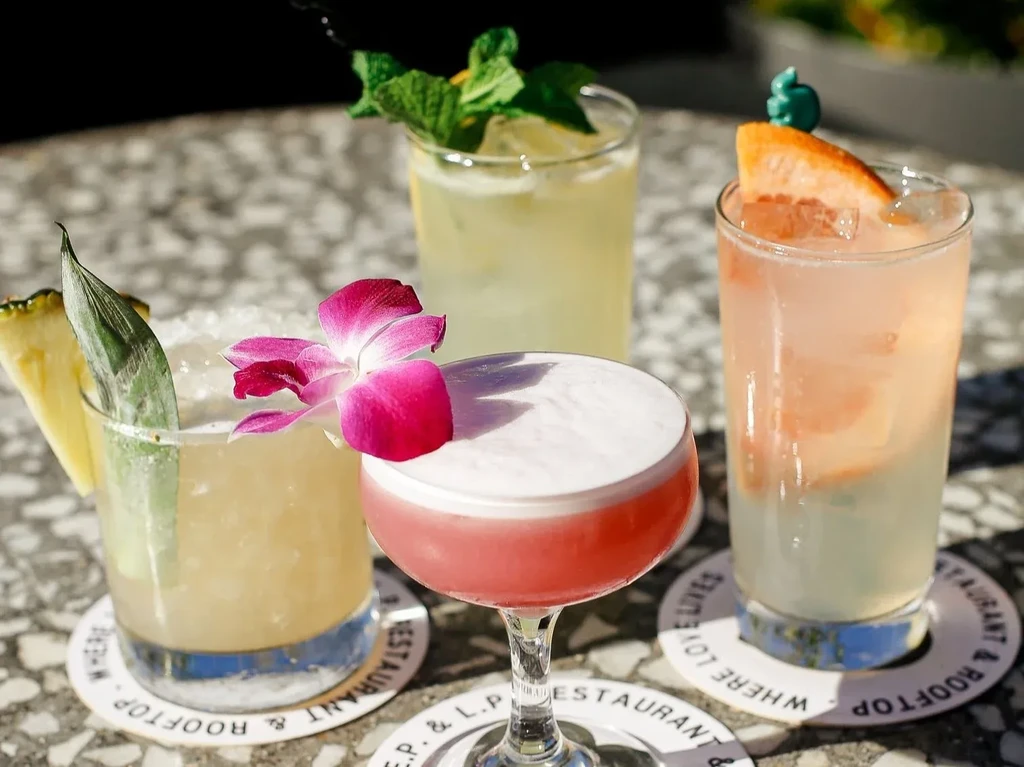 Four vibrant cocktails with diverse garnishes on an outdoor table.