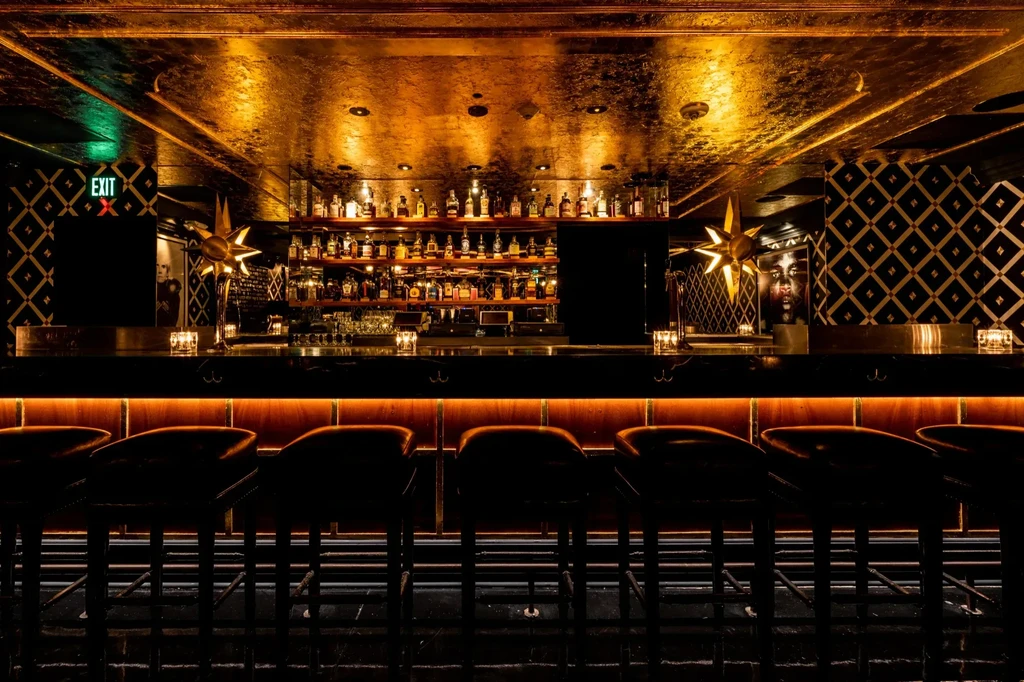 Luxurious bar with well-stocked counter, warm lighting, and reflective gold ceiling.