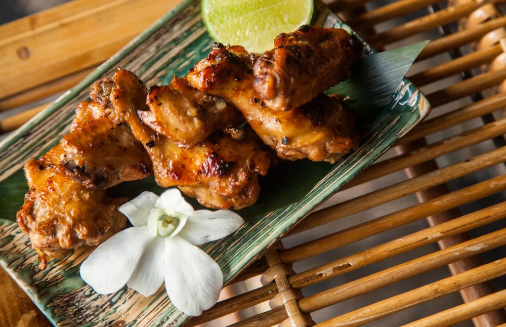 Golden-brown chicken pieces on a green plate with lime and orchid.