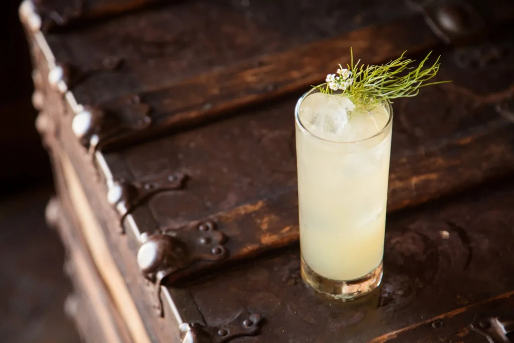 Pale drink with ice and flowers on a dark wooden chest.