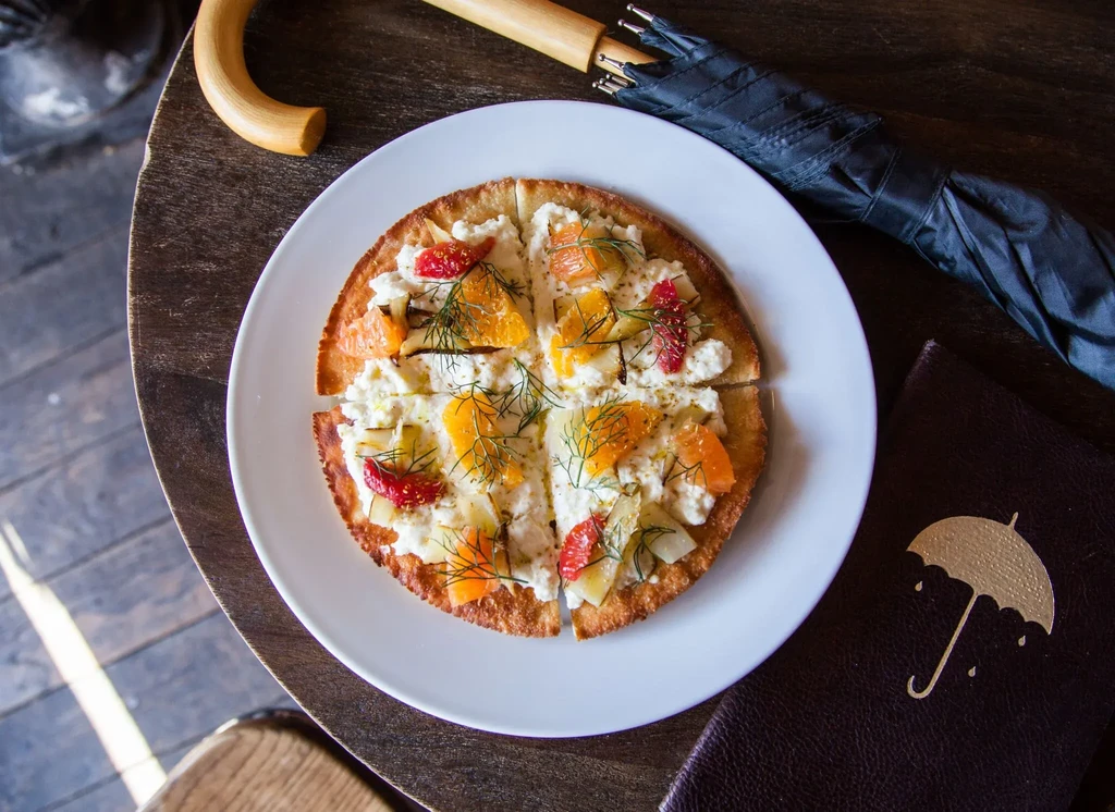 Savory flatbread with citrus, creamy cheese, and dill on a wooden table.
