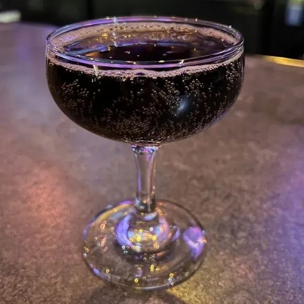 Dark, effervescent drink in a coupe glass, dimly lit.