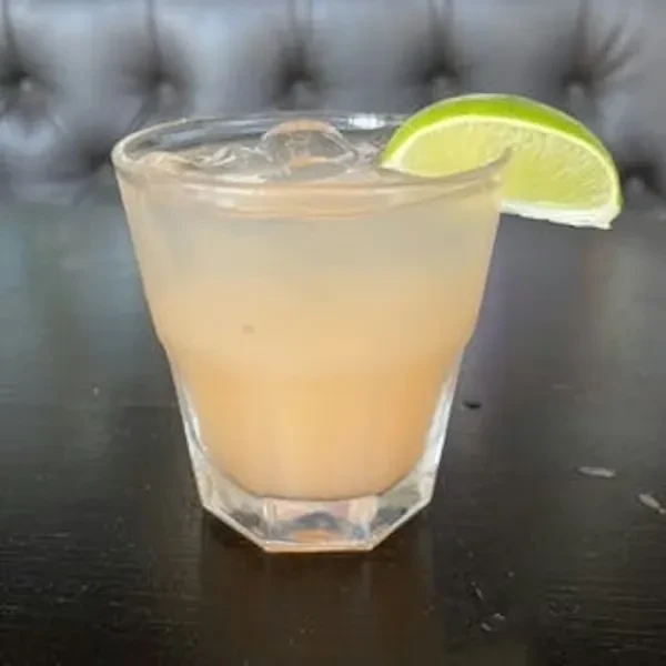 Cocktail in short glass with ice and lime on dark table.