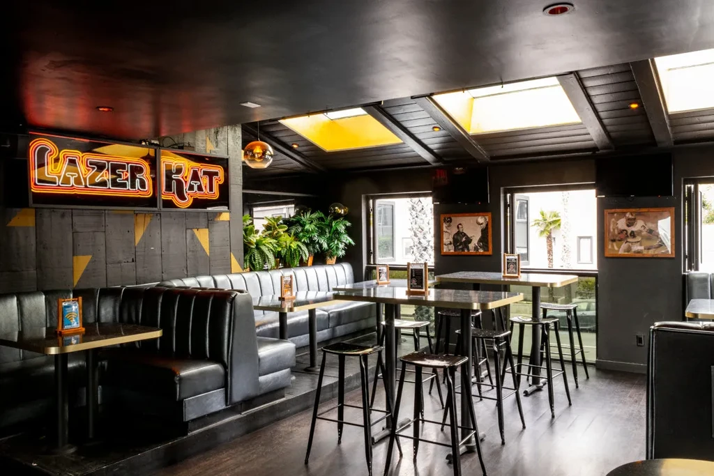 Dark, modern bar interior with "LAZER KAT" neon sign and booths.