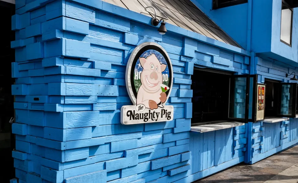 Blue textured building with "The Naughty Pig" sign and service windows.