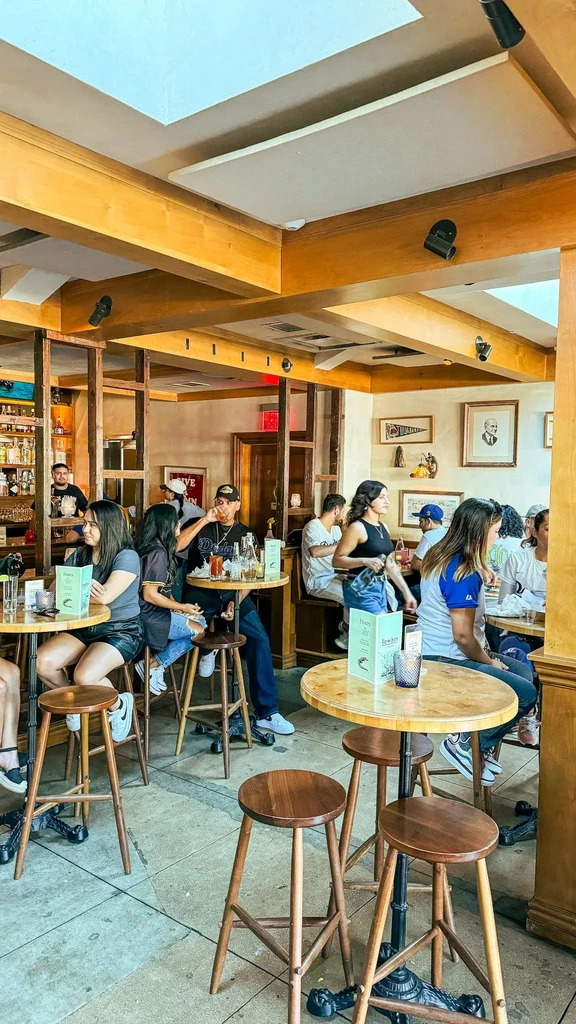Bustling wooden restaurant interior with high-top tables and a visible bar.