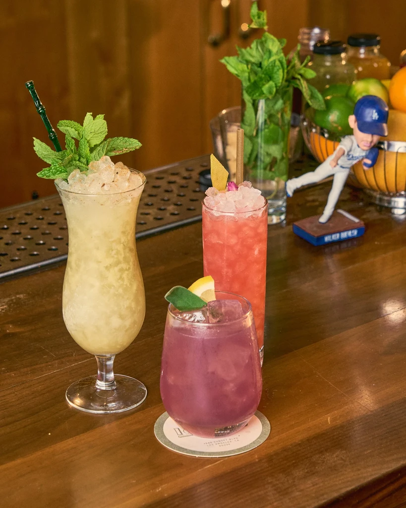 Three distinct garnished cocktails on a wooden bar counter.