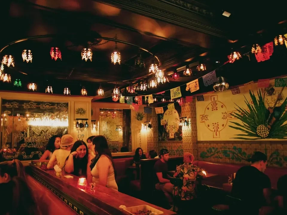 Warm, dimly lit bar with festive decor, murals, and visible patrons.