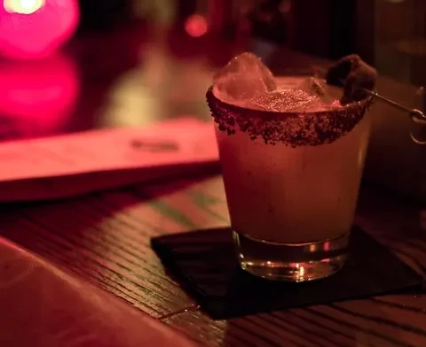 A red-hued cocktail with ice, dark garnish, and a coated rim.