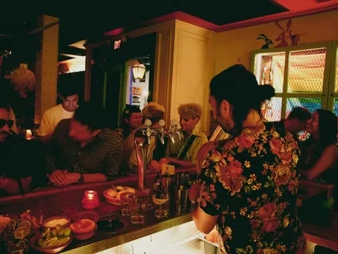 Lively, dimly lit bar scene with a bartender serving patrons.
