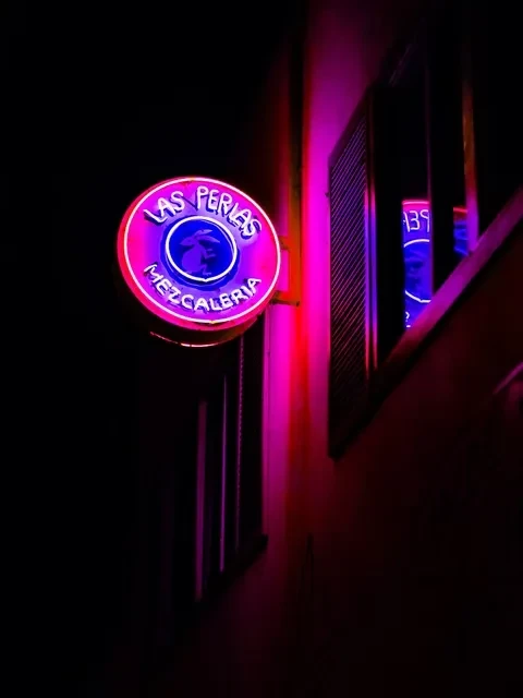 Vibrant neon sign for "LAS PERLAS MEZCALERIA" on a dark building.