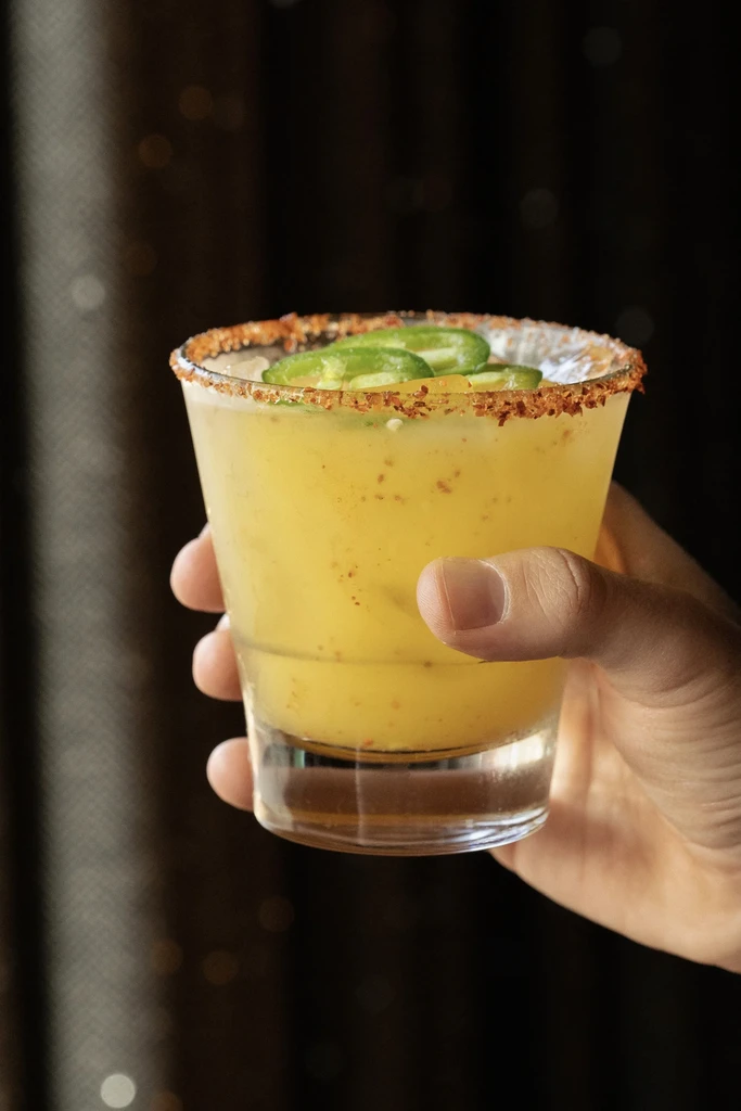 Close-up of a blended orange drink with jalapeño and spiced rim.