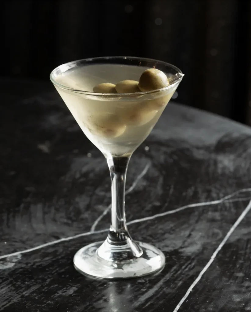 Close-up of a chilled martini with green olives on dark marble.