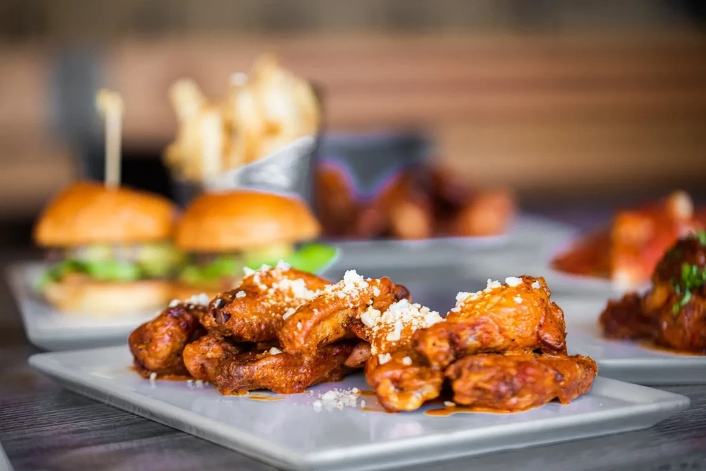 Close-up of crispy, sauced chicken wings with cheese, sliders, and fries.