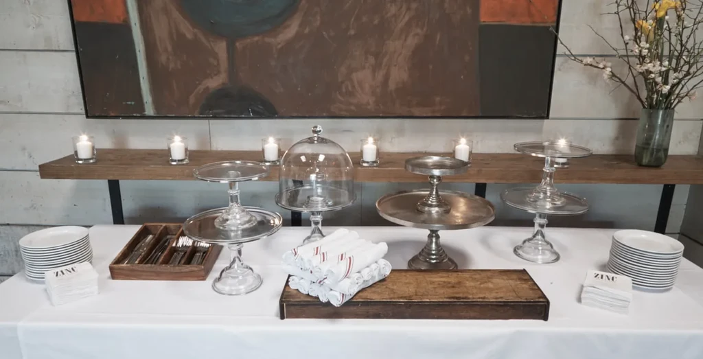 Empty buffet table with serving stands, plates, napkins, and lit candles.
