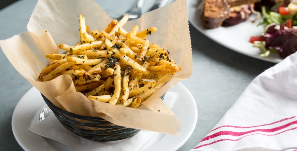 Close-up of crispy, herb-seasoned french fries in a black wire basket.