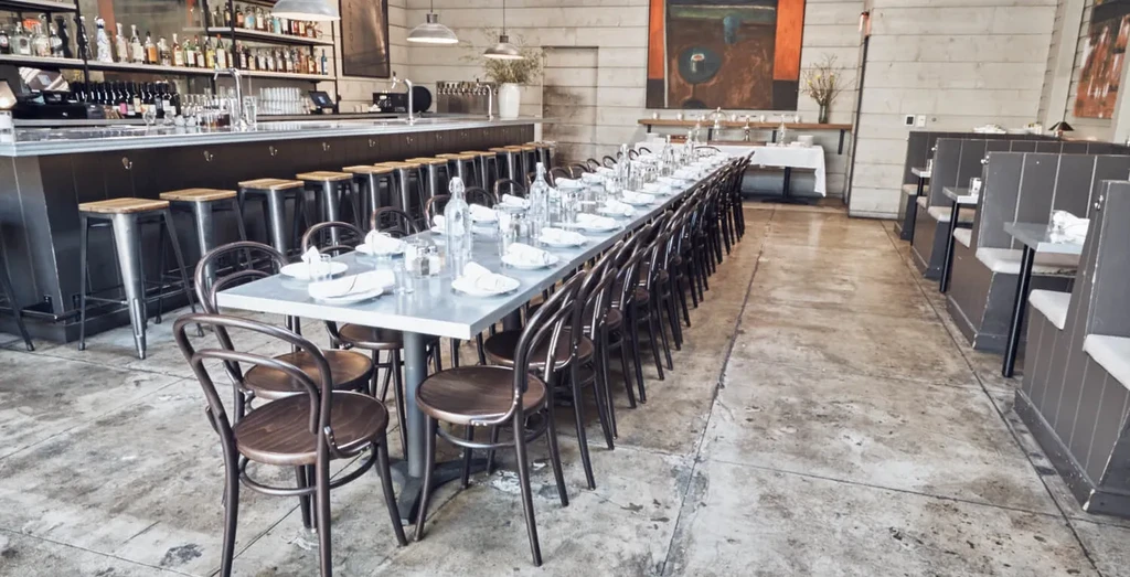 Empty modern restaurant interior with bar, communal table, and booths.