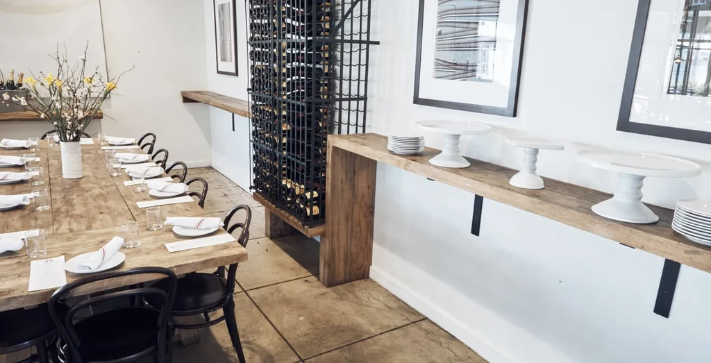 Modern rustic restaurant with set wooden communal table and wine rack.