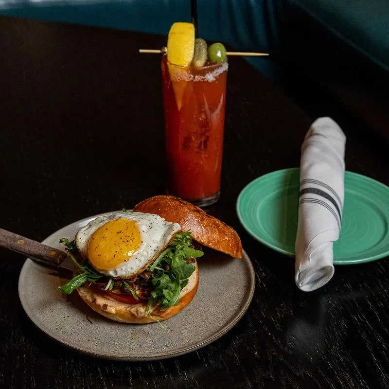 Burger with fried egg and arugula next to a garnished Bloody Mary.