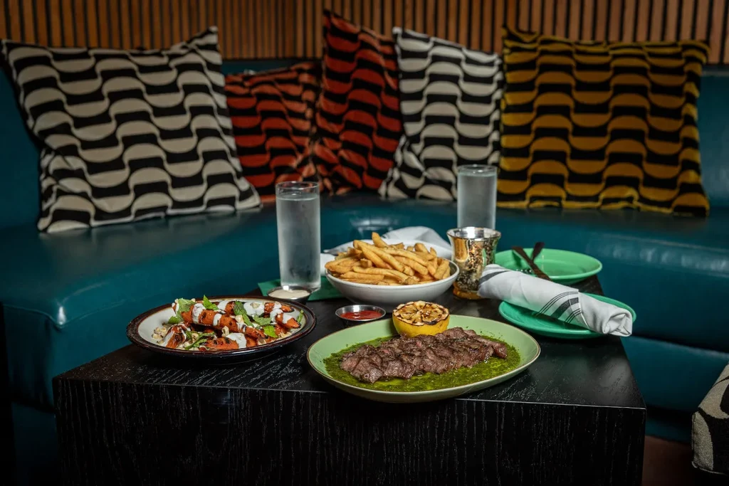 Grilled steak, fries, and vegetables on a modern restaurant coffee table.