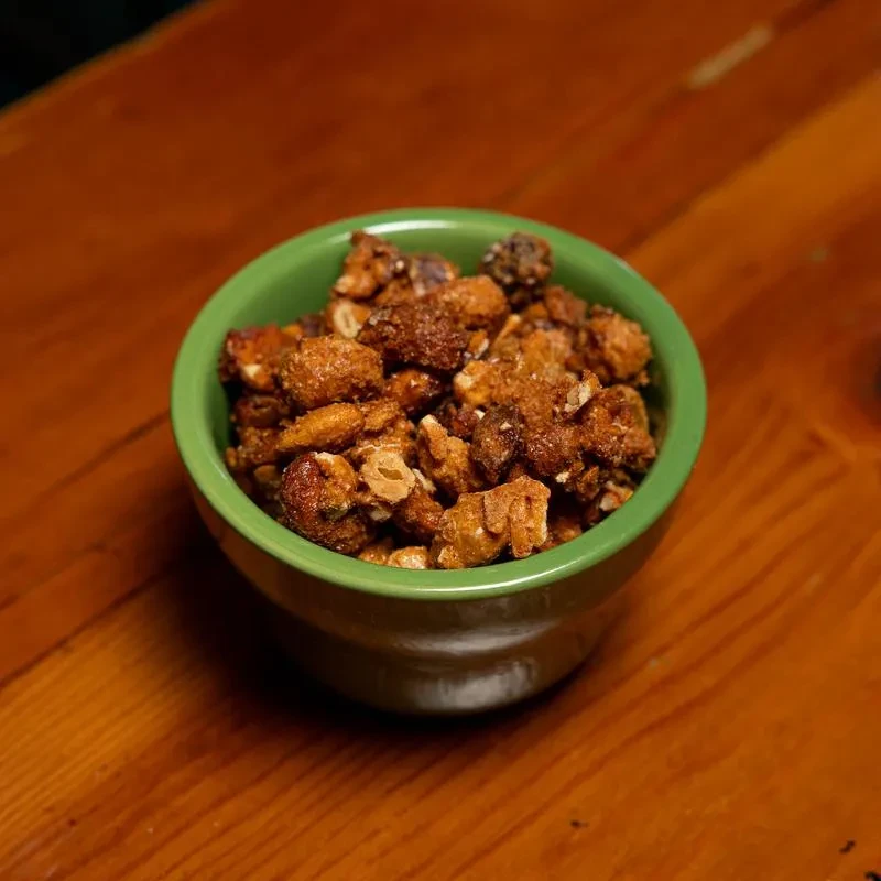 A green bowl of savory caramelized nuts on a wooden table.