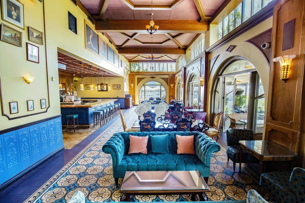 Ornate, empty restaurant interior with a bar and teal velvet sofa.