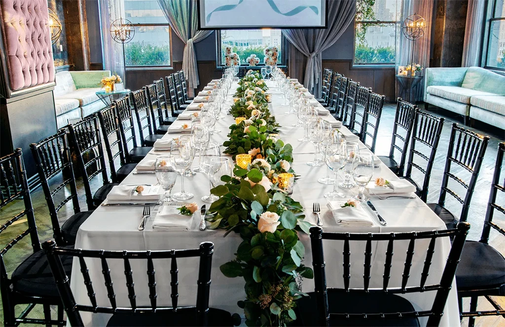 Elegant dining table with floral garland, candles, and Chiavari chairs.