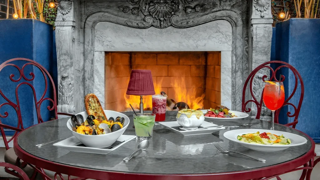 Elegant restaurant table with diverse dishes, colorful cocktails, and a warm fireplace.