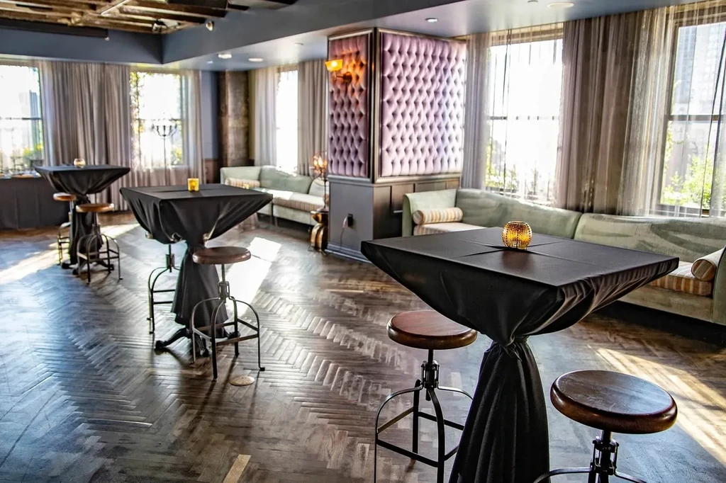 Elegant lounge with high-top tables, banquettes, and purple tufted pillar.