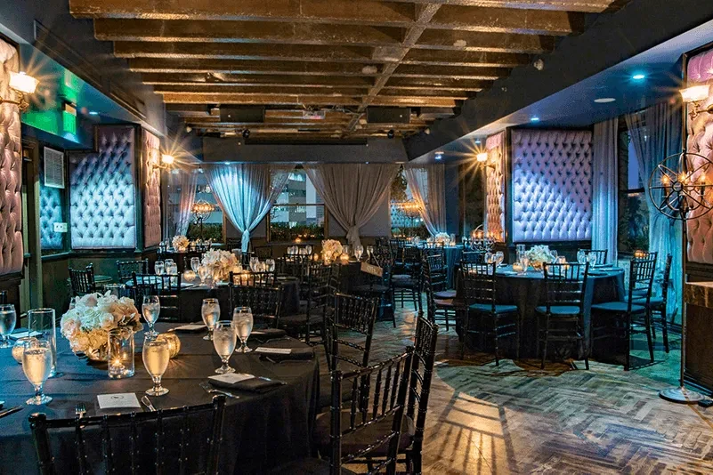 Upscale restaurant interior with black tables, floral centerpieces, and tufted walls.