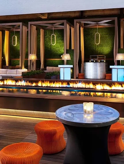 Modern outdoor lounge with fire pit, orange ottomans, and cabana sections.